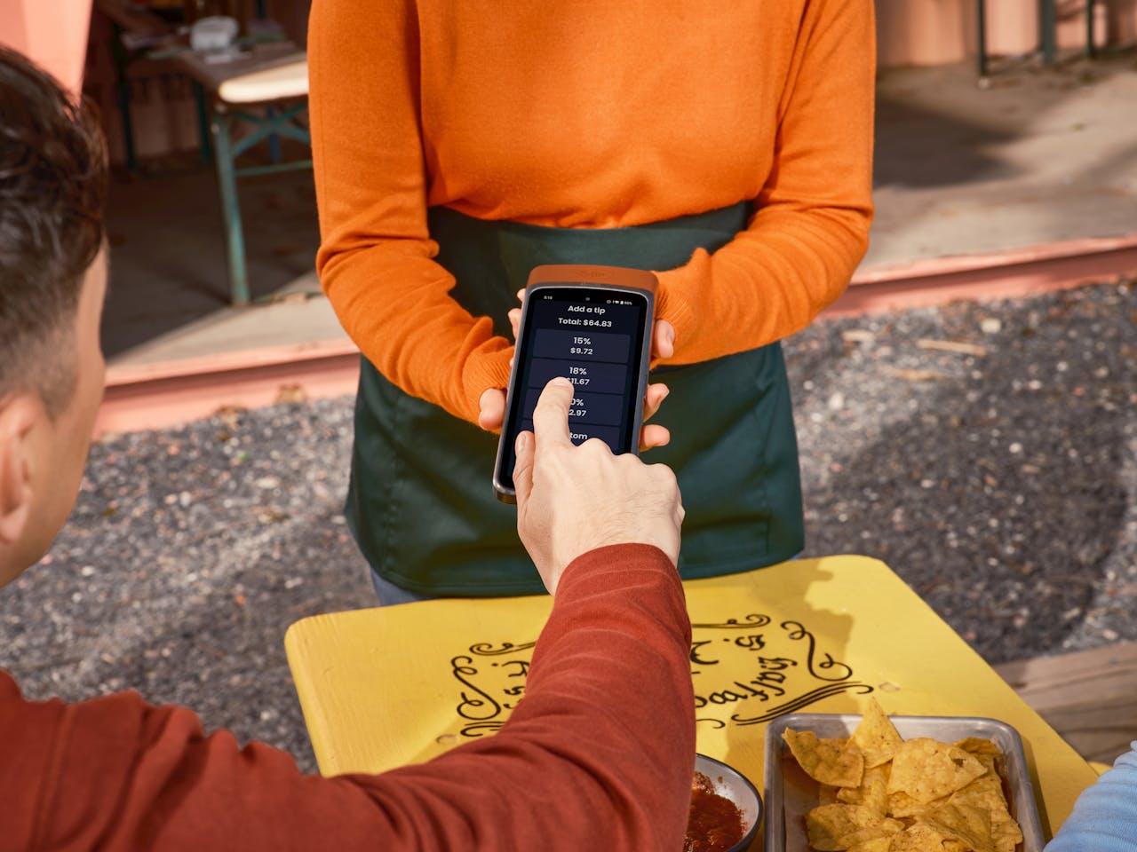 Person using phone for tipping at an outdoor dining table, highlighting contactless payment convenience.