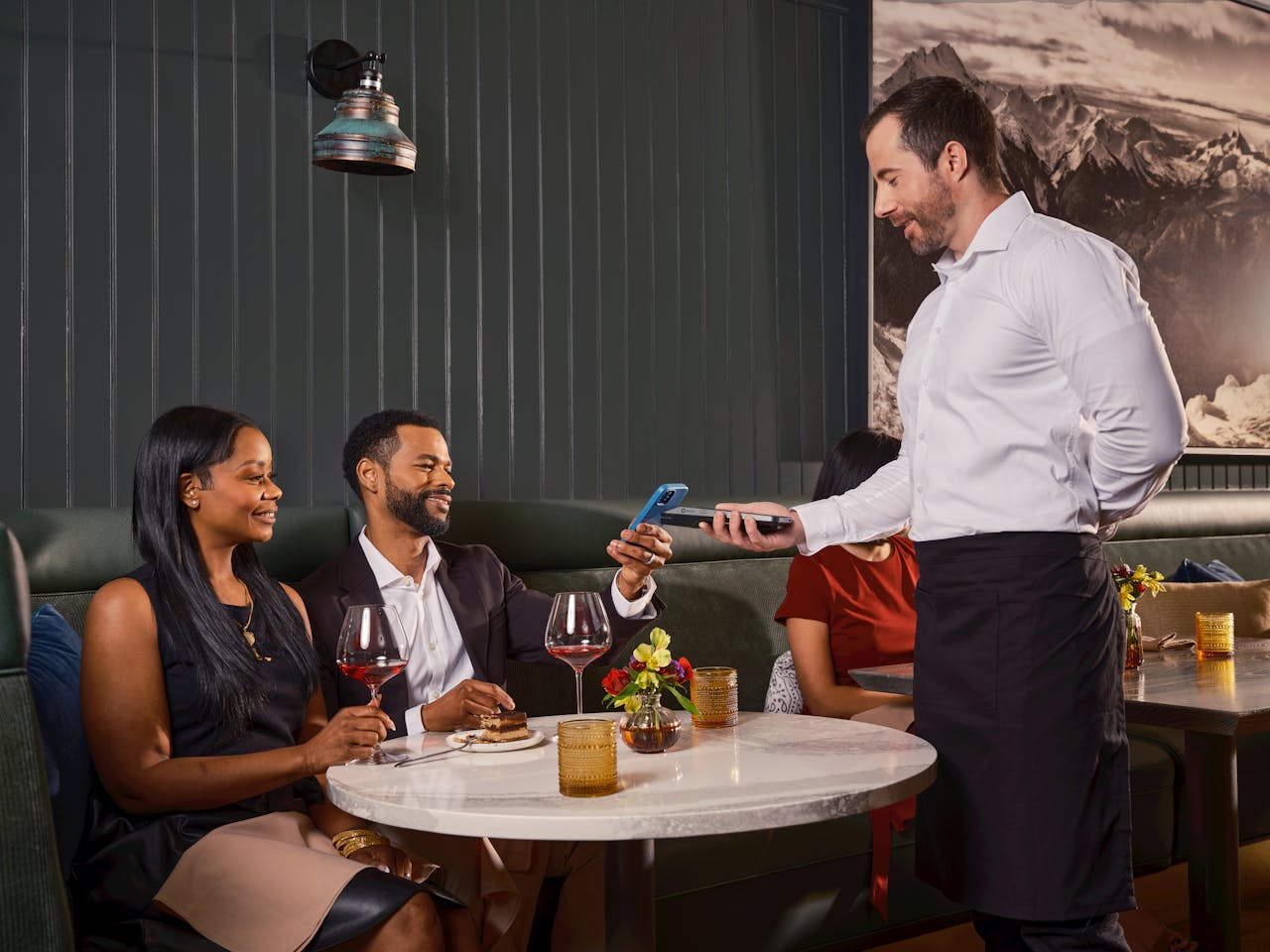 Diners complete a contactless payment in a sophisticated restaurant with a handheld POS system.