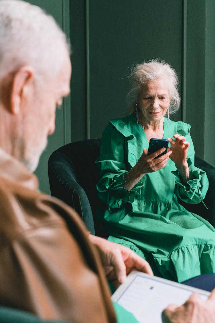 A senior couple using a smartphone and tablet together while sitting indoors, smiling.